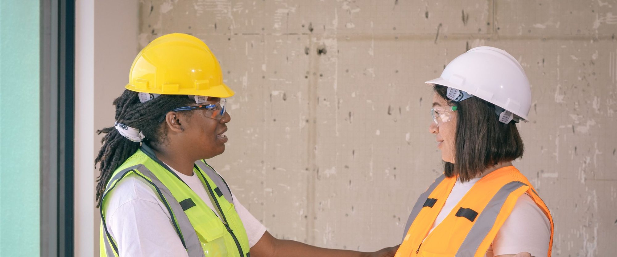 Two engineers in hard hats and high-visibility vests greeting each other on site