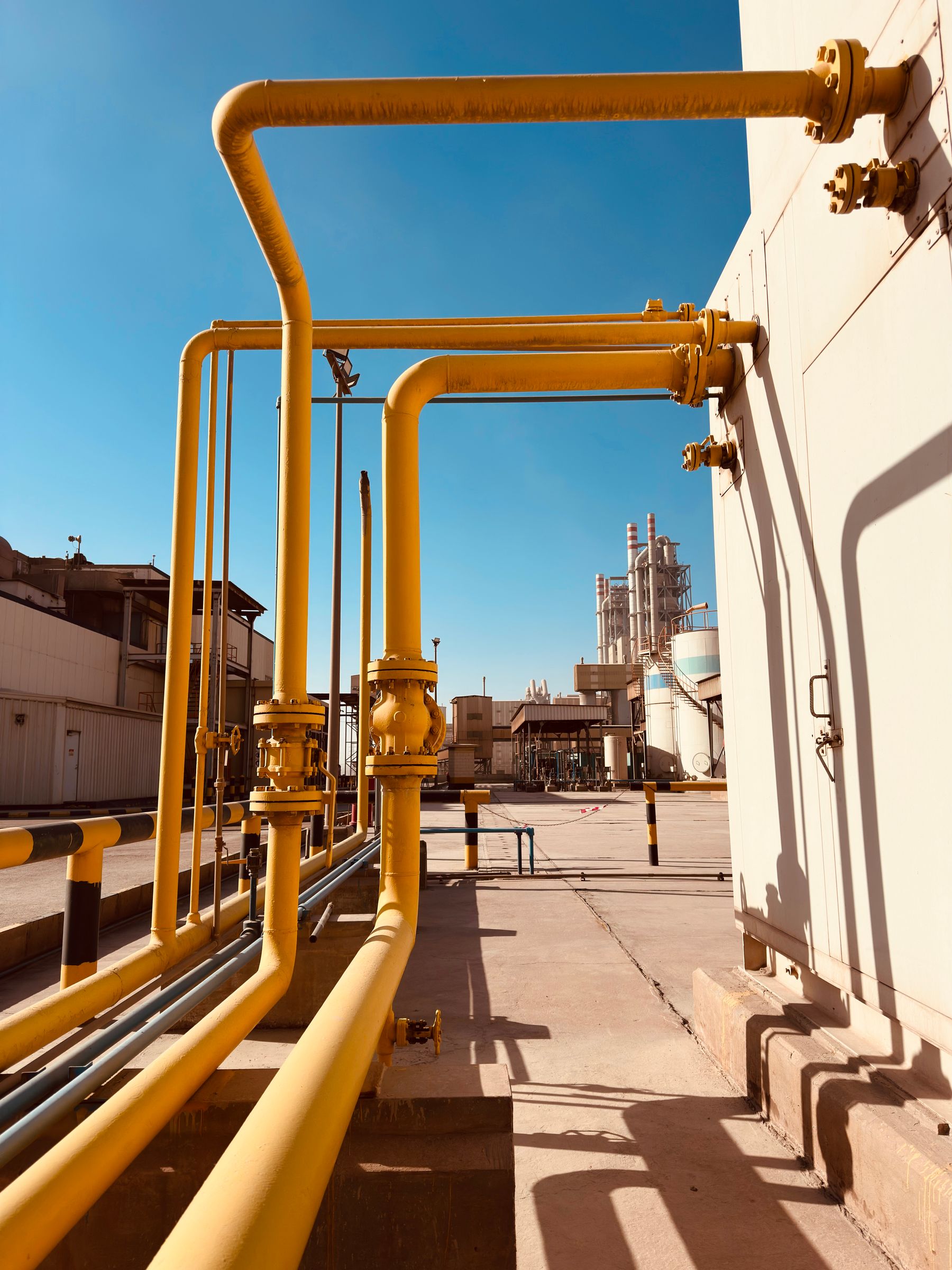 Yellow gas pipework and valves at a natural gas processing facility, set against a clear blue sky