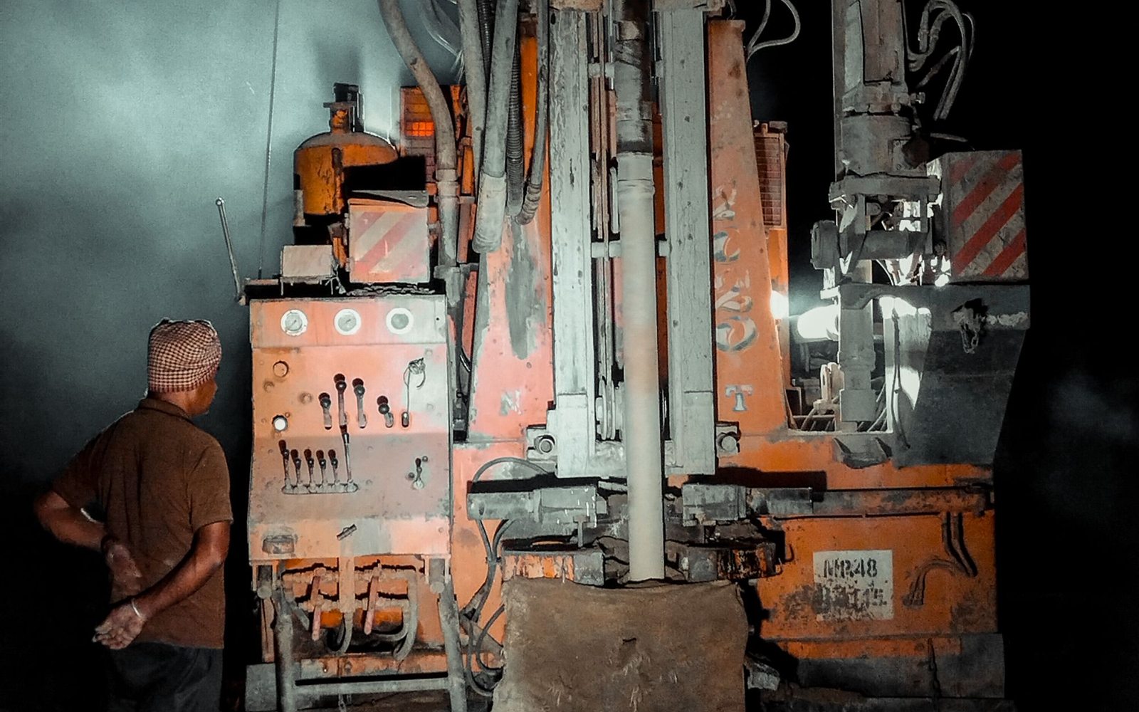A worker beside a borehole drilling rig at night