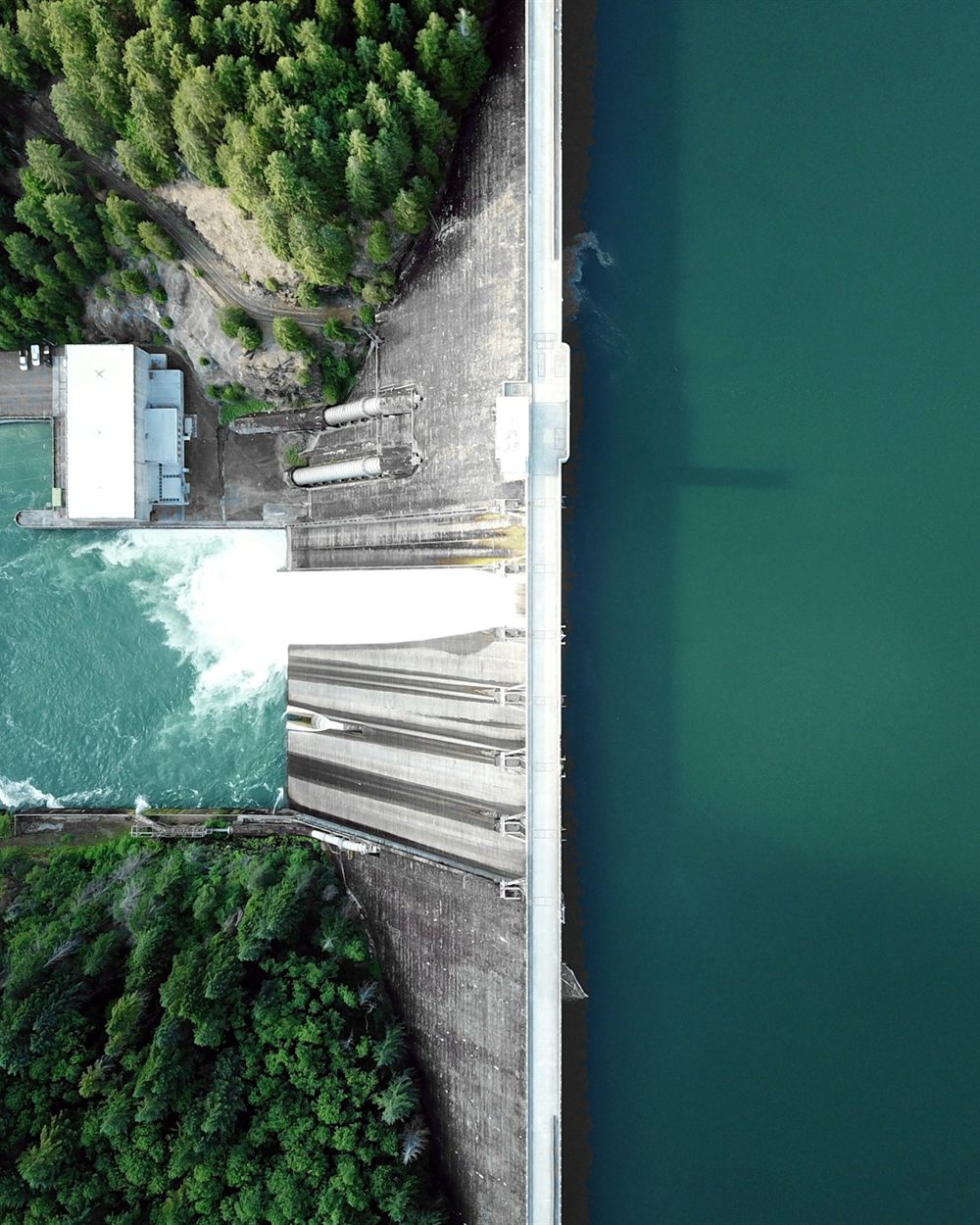 Aerial view of a concrete dam releasing water from a turquoise reservoir into a river