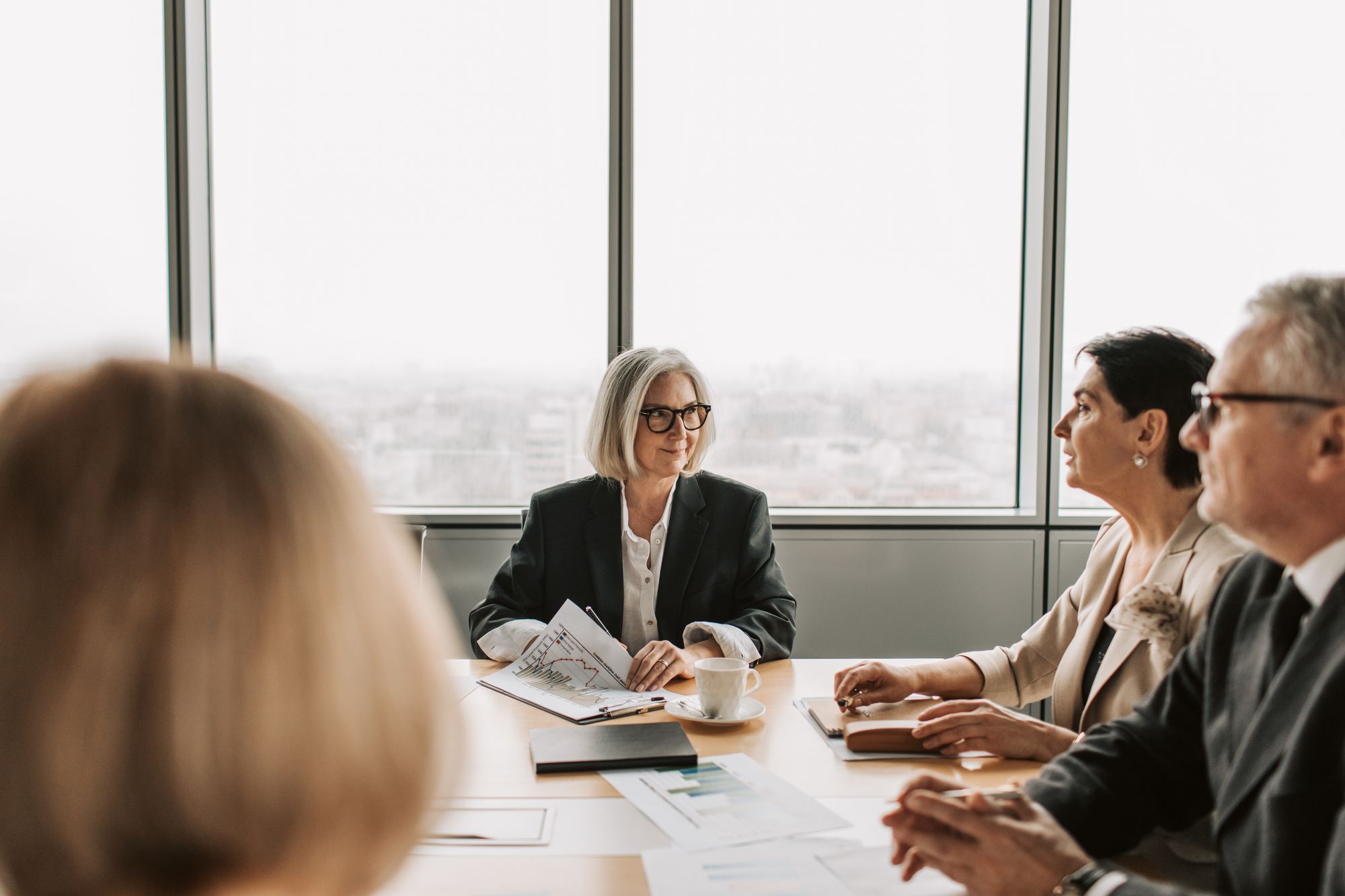 Professionals in a high-rise boardroom meeting with city views behind them